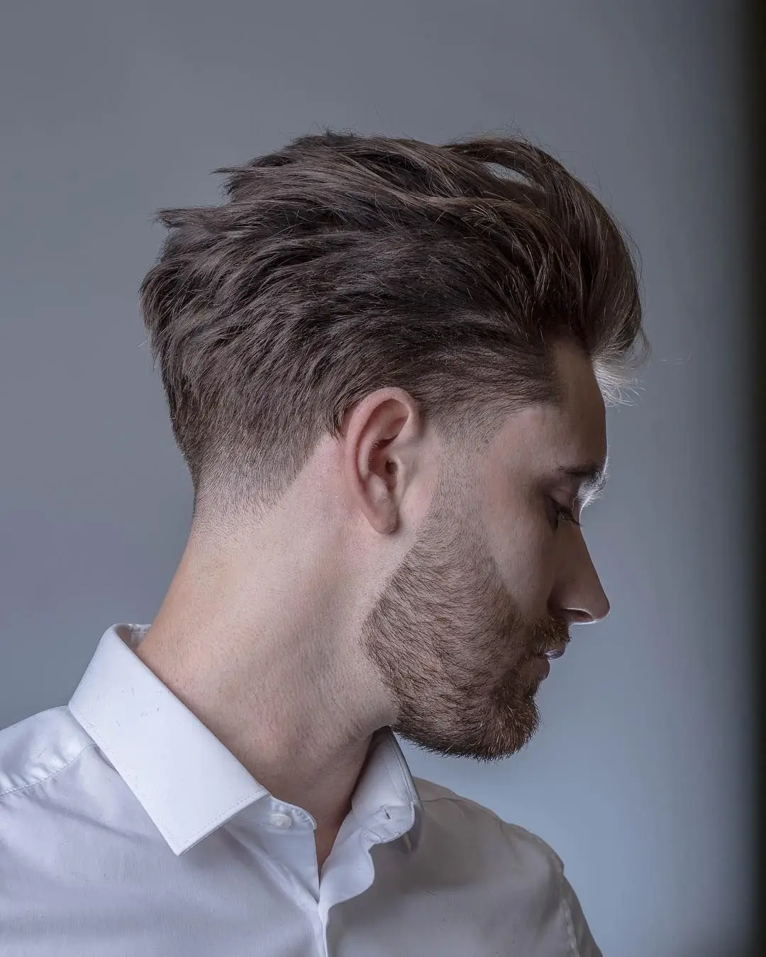 when the barber comes to you Side view of a person with a styled haircut and trimmed beard, wearing a white shirt.