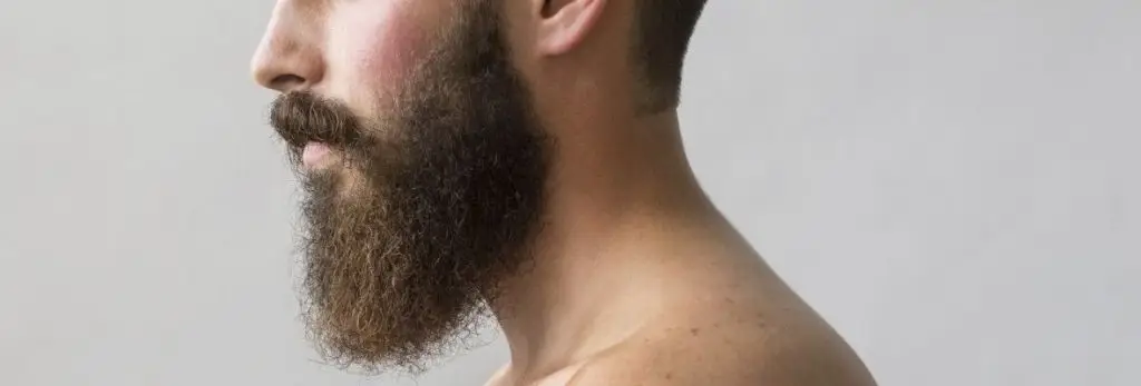 Side profile of a man with a full beard and bare shoulder on a light background